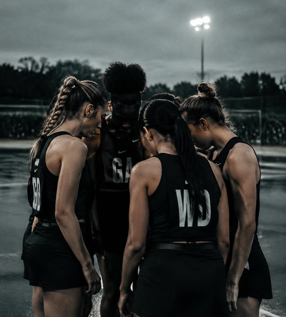Netball team in a huddle on an outdoor court at dusk